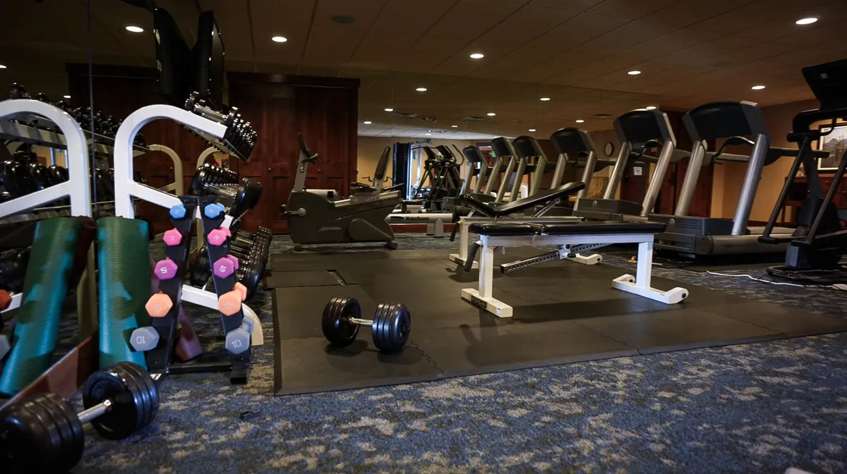 A well-equipped fitness center featuring treadmills, dumbbells, benches, and mats, all set in a bright, motivating space. The setup supports both solo workouts and group fitness, underscoring the versatility of on-site amenities for active guests.