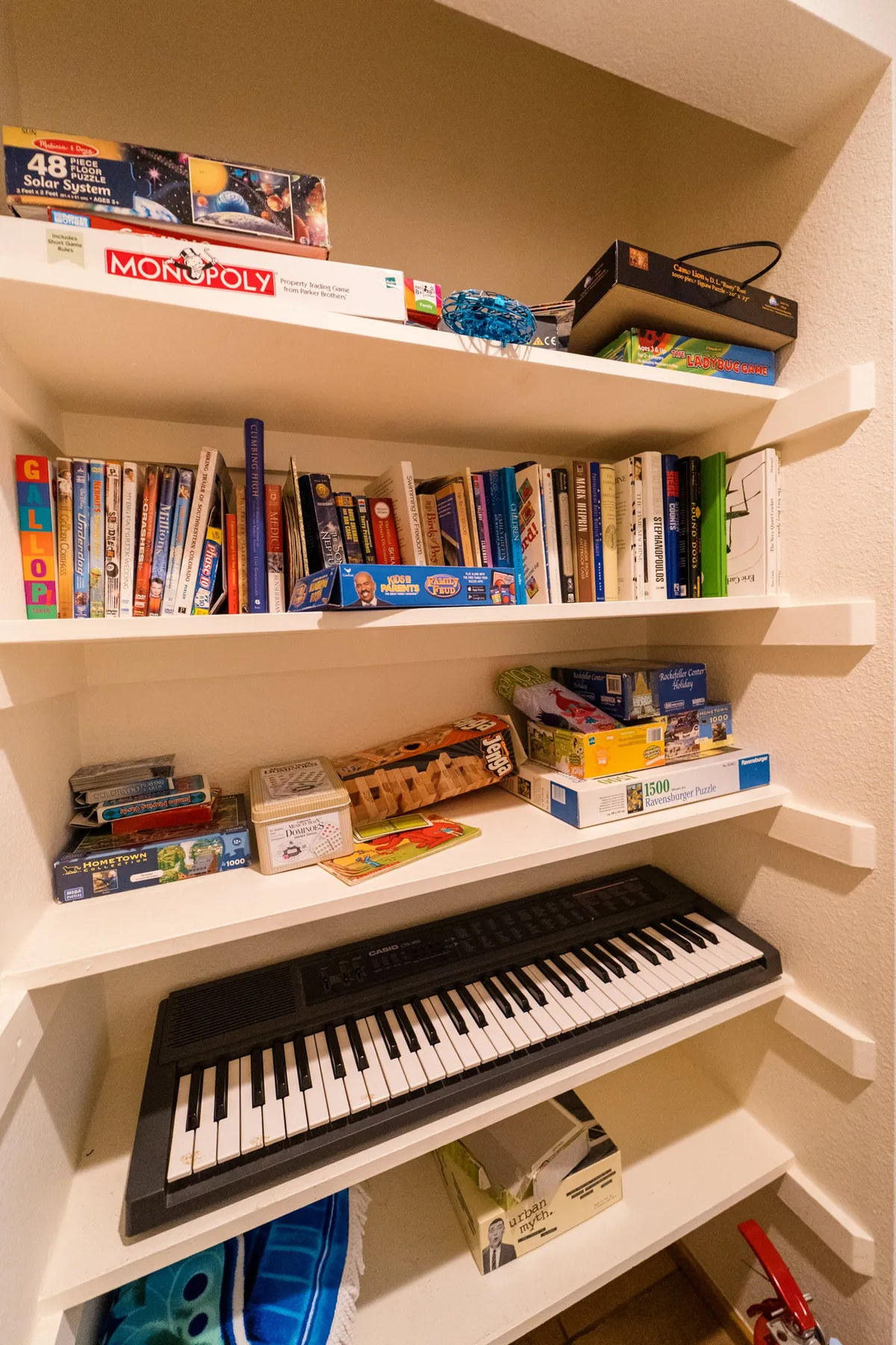 An interior image showing shelves filled with board games, books, and a keyboard, evoking playful family time and the creation of lasting memories indoors. The scene is colorful, organized, and inviting, suited for all ages.