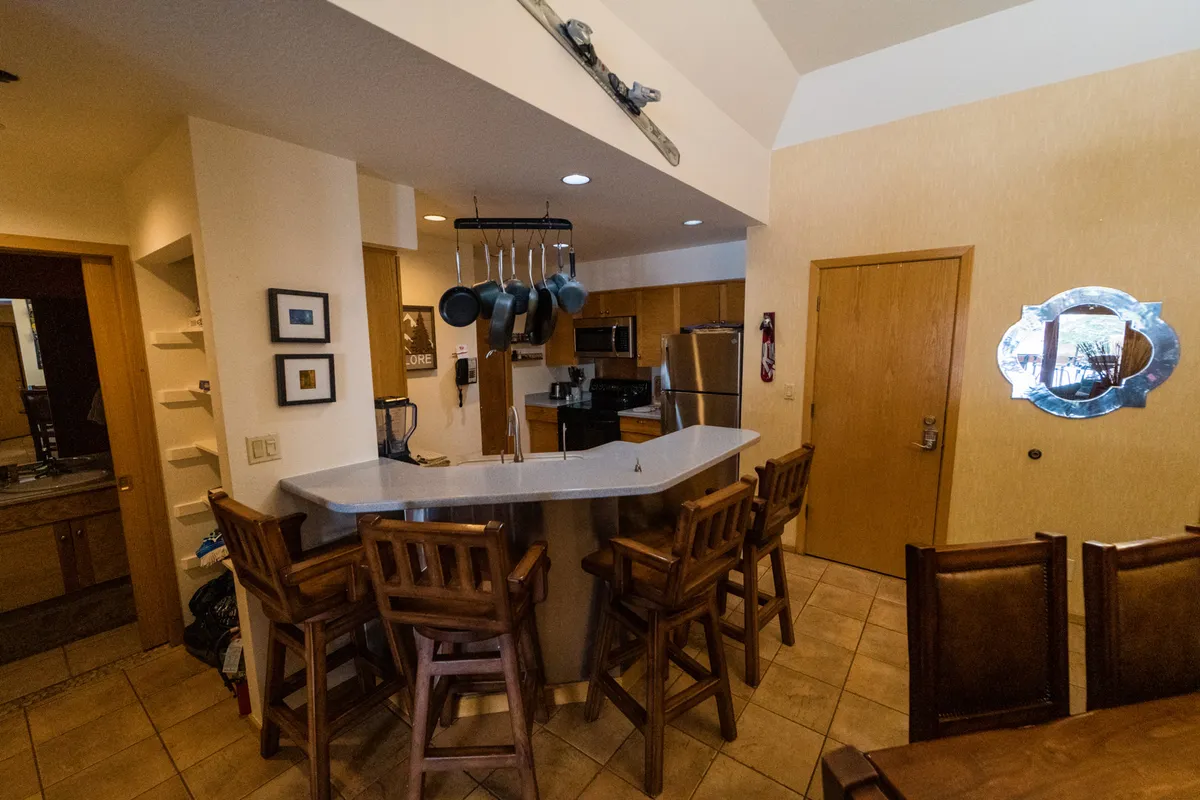 A cozy, inviting kitchen with a prominent island, bar stools for casual dining, hanging pots above, and high-end appliances visible along the counters. The decorative mirror and thoughtful design touches add to the upscale, homey feel. The space is open and seamlessly connected to the rest of the living area, ideal for both preparing meals and entertaining.