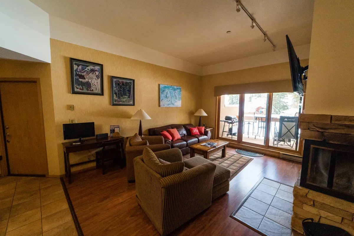 A comfortable living area featuring a sofa, coffee table, and fireplace, all framed by large windows that open up to mountain views. The space is inviting and functional, ideal for relaxing, socializing, or setting up a remote workspace with stunning scenery.