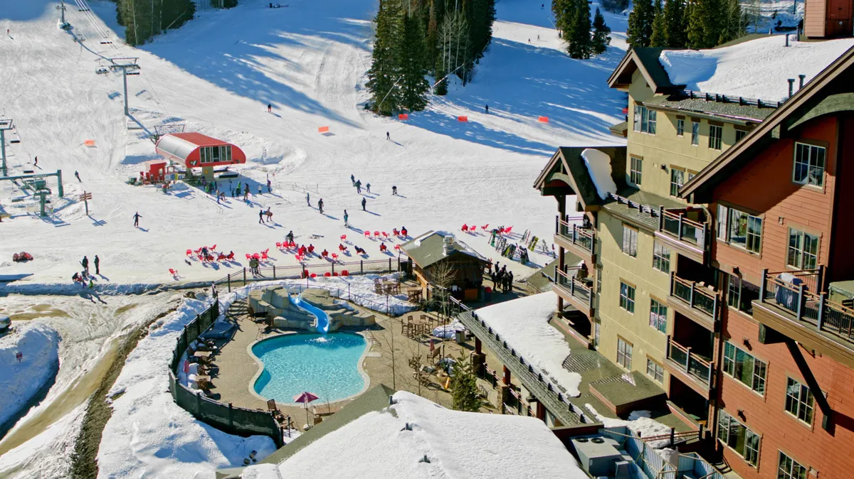 This vibrant exterior image features snow-covered ski slopes, visible chair lifts, a lively pool area, and lodge buildings nestled among pine trees. People are seen enjoying a mix of activities including skiing, swimming, and socializing, capturing the energy of après-ski life.